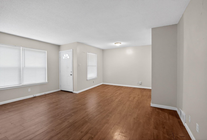 Spacious interior featuring wood-finish flooring, light neutral wall tones, white trim, and multiple windows with blinds
