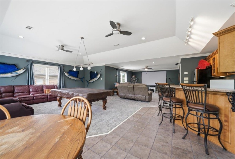 Spacious entertainment area featuring a built-in bar with stone-look countertops, tile flooring, recessed lighting, and multiple ceiling fans