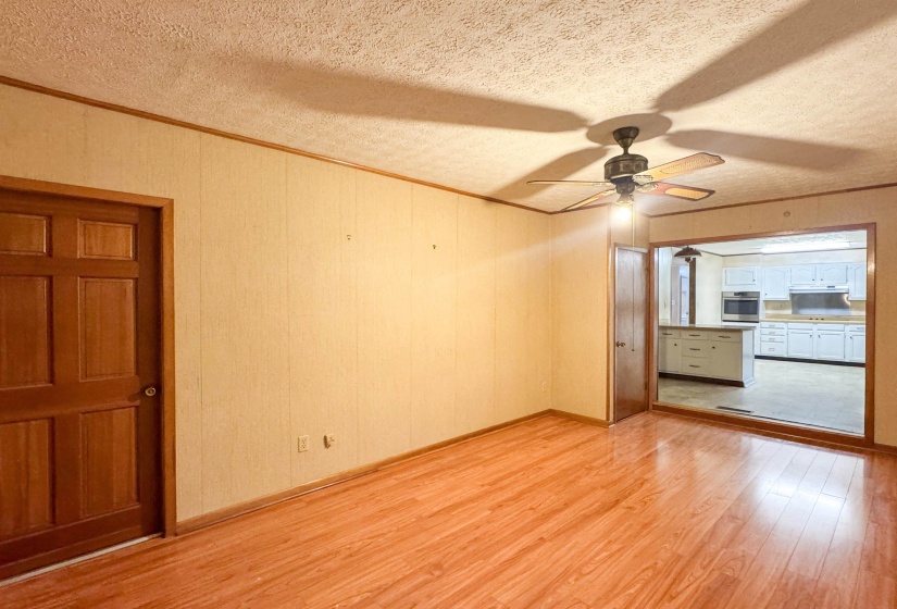 Spacious dining room with wood laminate flooring, light-toned textured wall paneling, and a ceiling fan.