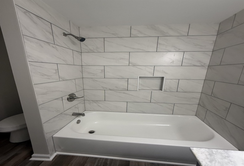 Tub and shower combination featuring a contemporary showerhead, white subway tile surround with gray veining, recessed niche, and polished chrome fixtures