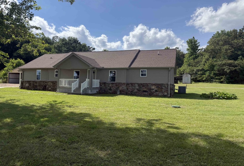 Ranch-style residence featuring a covered front porch, stone and siding exterior, asphalt shingle roof, and a gravel driveway leading to a detached carport