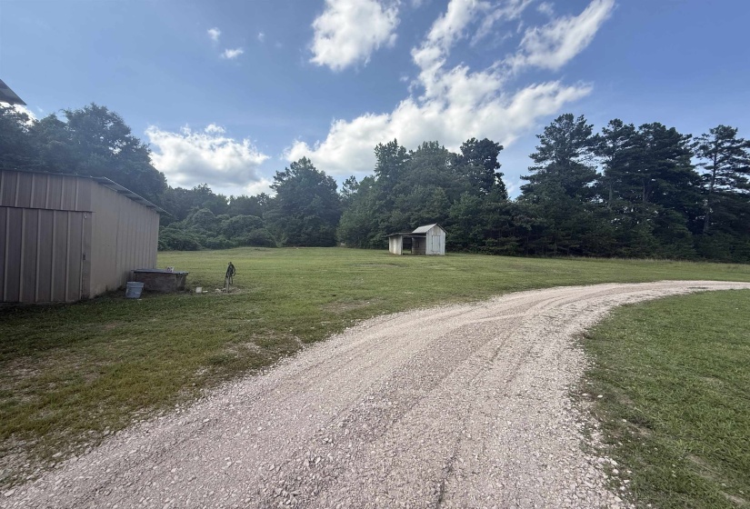 Gravel drive leading to a metal-sided utility building and a smaller detached shed