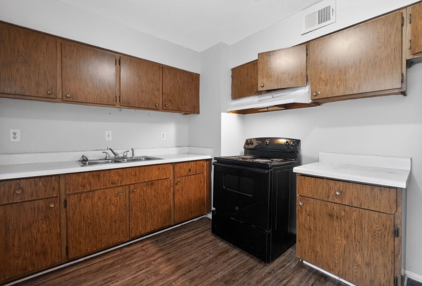 Kitchen featuring black / electric stove, light countertops, under cabinet range hood, dark wood finished floors, and brown cabinets