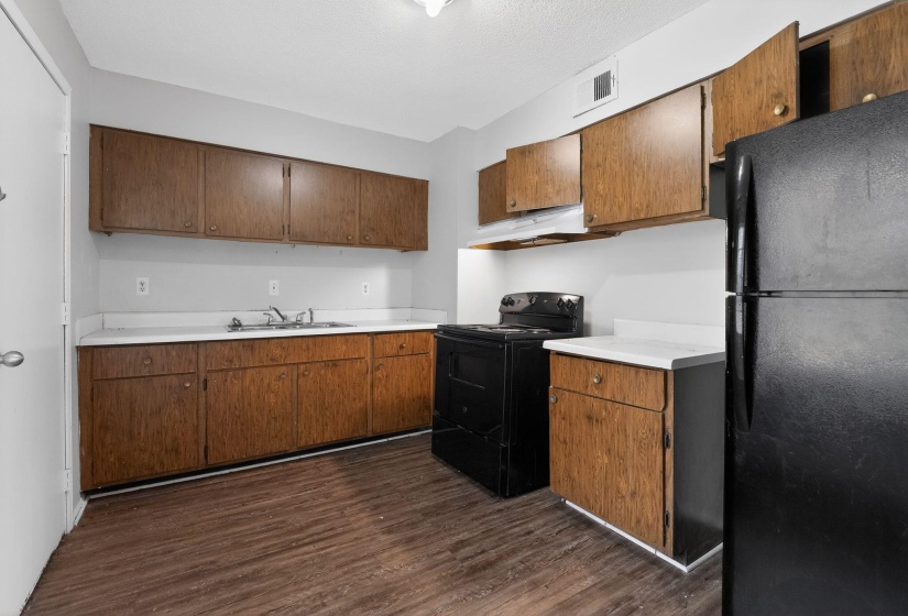 Kitchen with light countertops, black appliances, brown cabinets, dark wood finished floors, and a textured ceiling