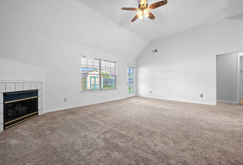 Spacious living area featuring a vaulted ceiling with a ceiling fan, a fireplace, neutral carpeting, and freshly painted.
