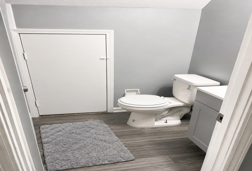 Full bathroom featuring wood-finish flooring, light gray walls, a white toilet, and a vanity with a white countertop and gray cabinetry