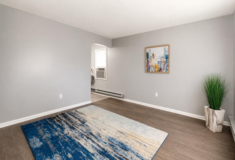 Spacious room featuring wood-finish flooring, light grey painted walls, white baseboards, and a bright window in the background