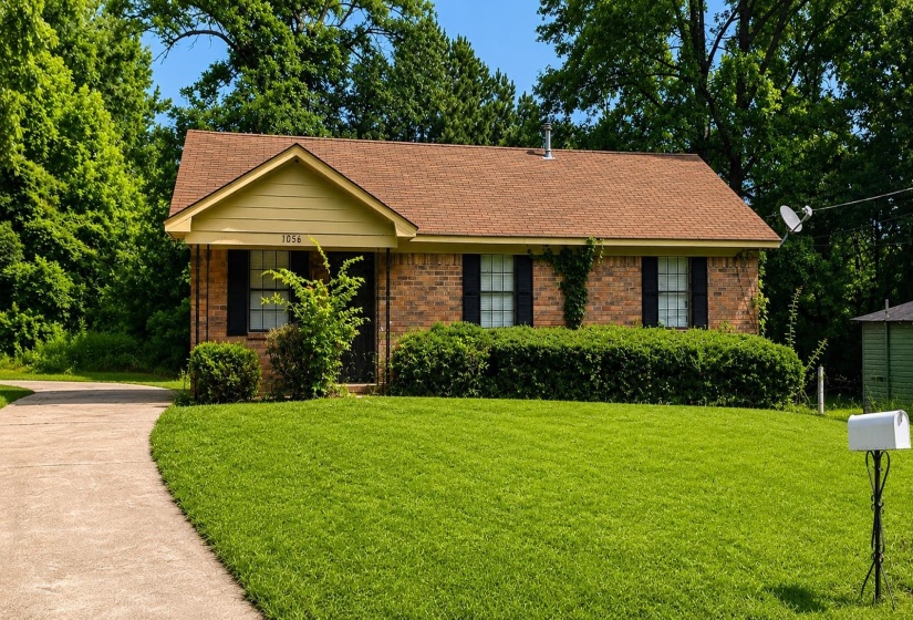 Brick facade residence featuring a front gable, brown shingle roof, dark window shutters, and a manicured lawn