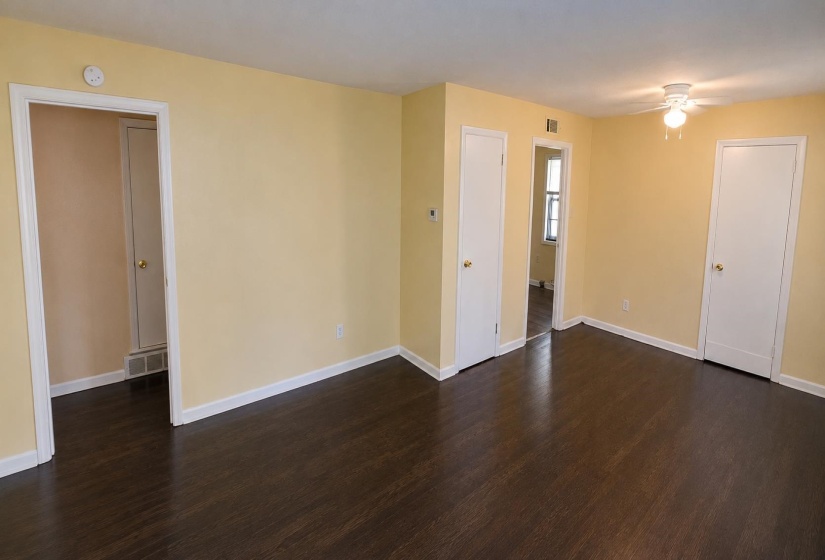 Spacious room featuring dark wood-finish flooring, light-toned walls, multiple doorways, and a ceiling fan with integrated lighting