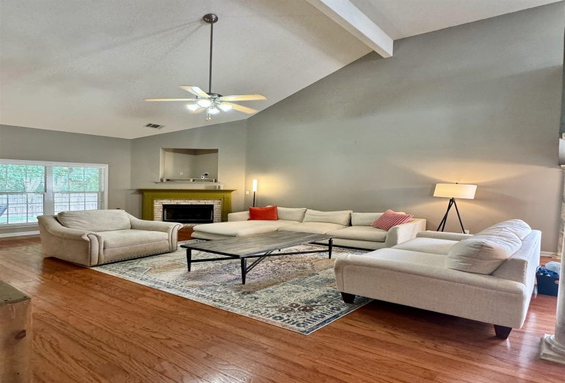 Spacious living area featuring vaulted ceilings with exposed beams, wood-finish flooring, and a fireplace with a decorative mantel