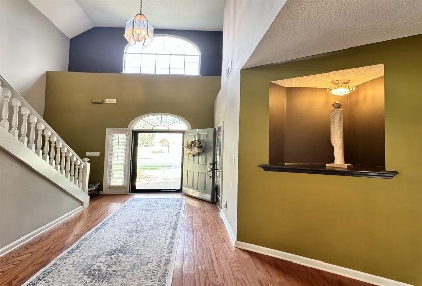 Two-story foyer featuring wood-finish flooring, a decorative staircase with white balusters, and a transom window above the main entry