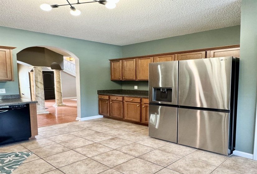 Kitchen featuring tile flooring, wood cabinetry, dark countertops, and stainless steel refrigerator