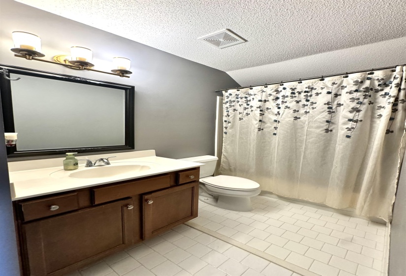 Bathroom featuring a wood-finish vanity with an integrated sink and light-toned countertop, a framed mirror, and a three-light vanity fixture