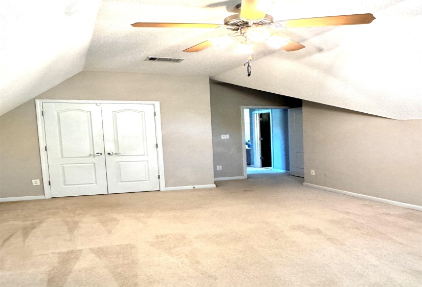 Carpeted room with sloped ceilings, featuring a ceiling fan with light fixture, double panel doors, and a recessed doorway