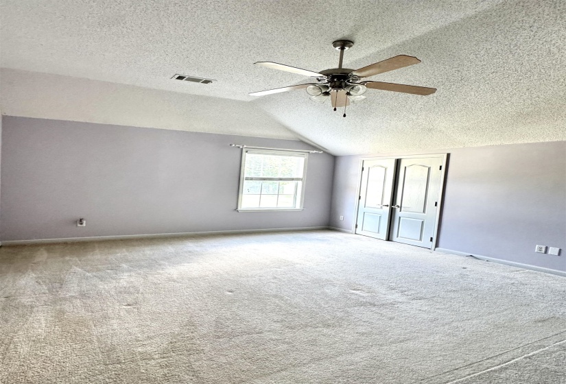 Spacious room featuring vaulted ceilings, a ceiling fan with light fixture, and neutral-toned wall-to-wall carpeting