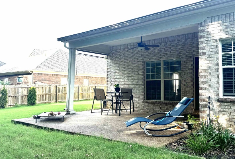 Covered patio with a ceiling fan, brick exterior, and a fenced backyard with mature landscaping