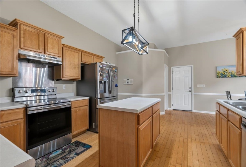 Kitchen featuring stainless steel appliances, light wood-finish cabinetry, solid surface countertops, a central island, and wood-finish flooring