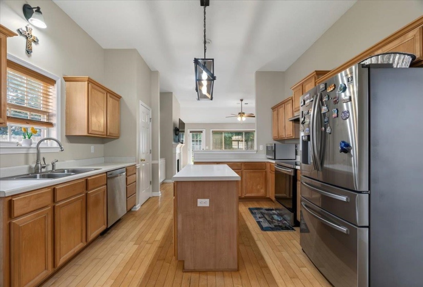Kitchen featuring wood-finish flooring, light wood cabinetry, stainless steel appliances, and a central island with a white countertop