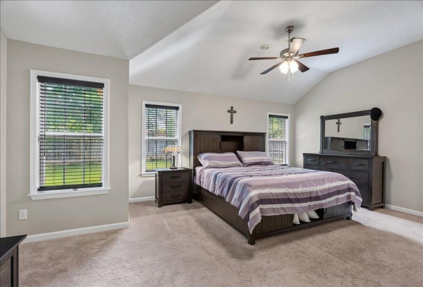Room featuring a vaulted ceiling, ceiling fan with light, two windows with blinds, and neutral carpet flooring