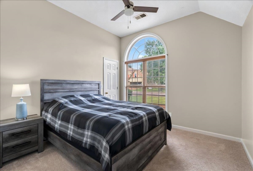 Vaulted ceiling with a ceiling fan, arched window with blinds, carpeted flooring, and a two-panel interior door