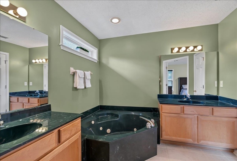 Bathroom featuring dual wood-finish vanities with dark countertops, a built-in jetted tub, recessed lighting, and a horizontal window