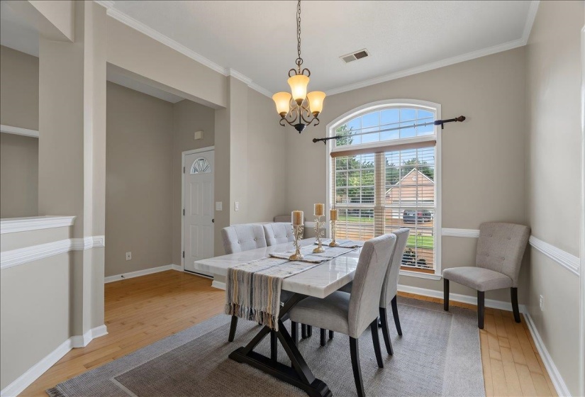 Dining area featuring an arched window, crown molding, chair rail molding, and wood-finish flooring
