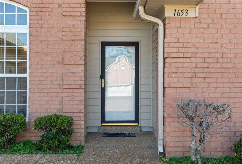 Brick exterior featuring a black frame storm door with decorative glass