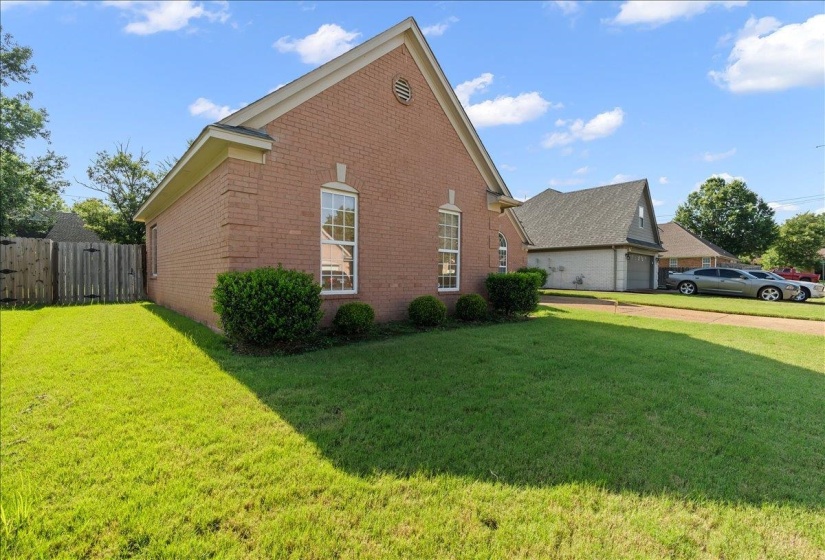 Brick exterior home featuring a gabled roofline, double-hung windows with white frames, and foundational shrubbery