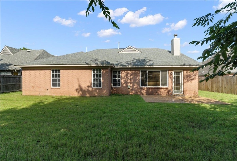Expansive backyard featuring a brick exterior, a large patio area, a white chimney, and a durable shingle roof