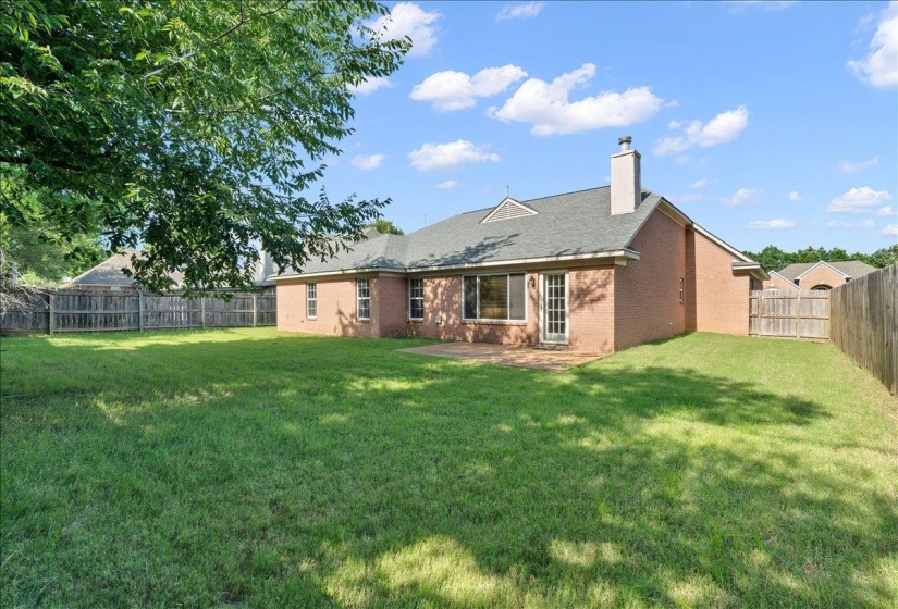 Expansive backyard featuring a manicured lawn, brick exterior, a patio area, and a privacy fence