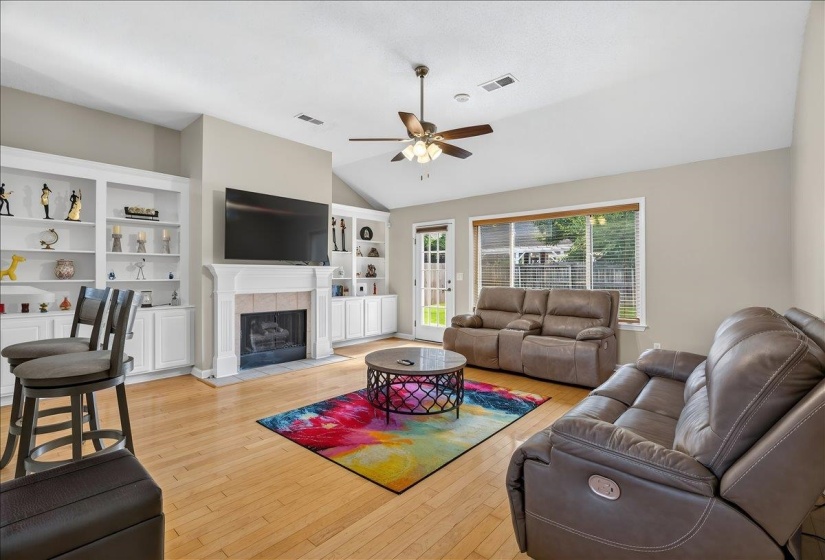 Spacious living area featuring light wood-finish flooring, a white mantel fireplace with tile surround, and built-in shelving