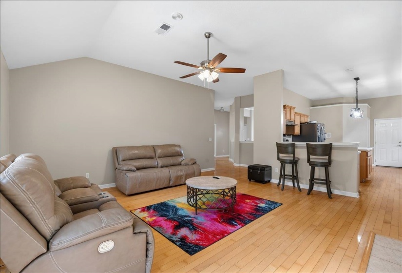 Open-concept living space featuring wood-finish flooring, vaulted ceiling, and an integrated kitchen bar with pendant lighting