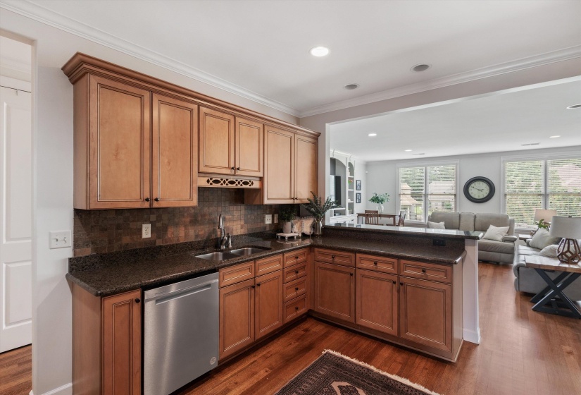 Kitchenette featuring wood cabinetry, dark countertops, an integrated sink, a stainless steel dishwasher, and tile backsplash