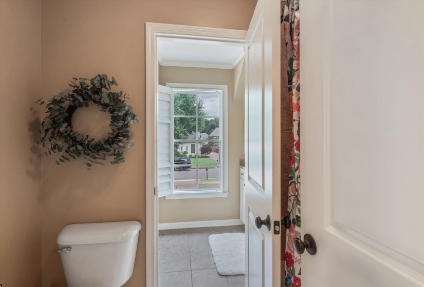 Windowed bathroom featuring white louvered shutters and tile flooring