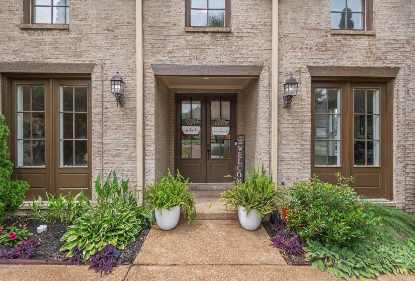 Brick facade featuring a covered entry with a glass-paneled door, flanked by two large glass-paneled windows