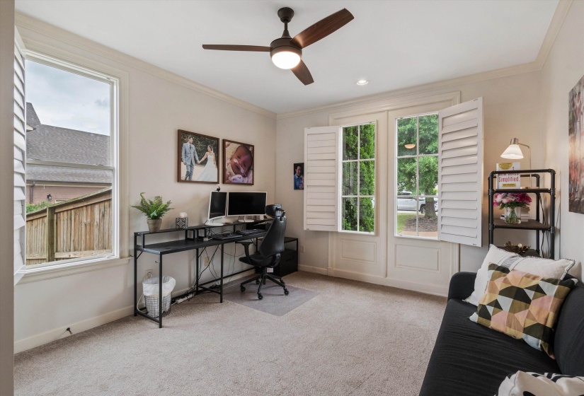 Carpeted room featuring a ceiling fan with integrated lighting, crown molding, and multiple windows with plantation shutters