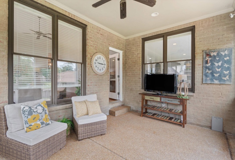 Covered outdoor patio featuring a neutral-toned brick exterior, a textured concrete floor, and multiple windows with blinds