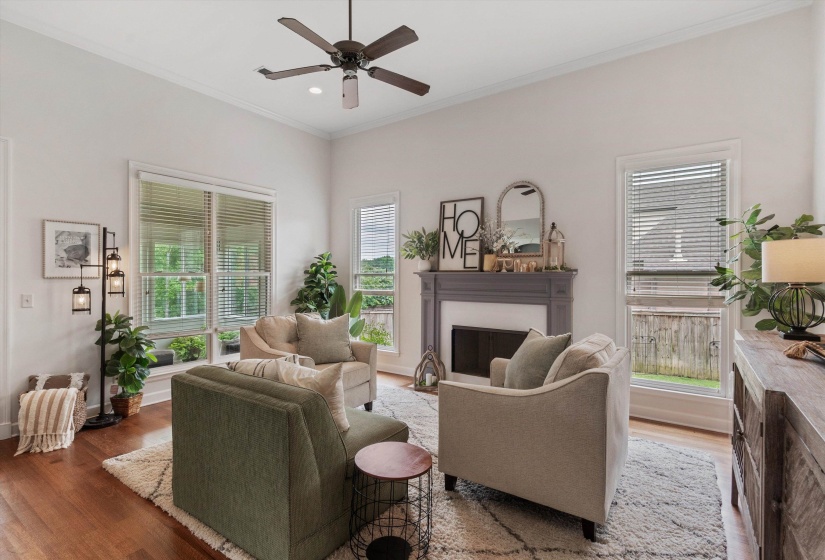 Living area featuring high ceilings with crown molding, a ceiling fan, a fireplace with a mantel, wood-finish flooring, and multiple windows