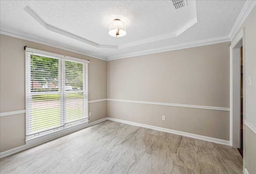 Room featuring light-toned walls with chair rail molding, a tray ceiling with crown molding, and wood-finish flooring