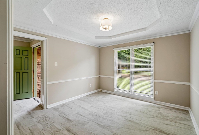 Spacious room featuring wood-finish flooring, a tray ceiling with a central light fixture, and a large window with blinds