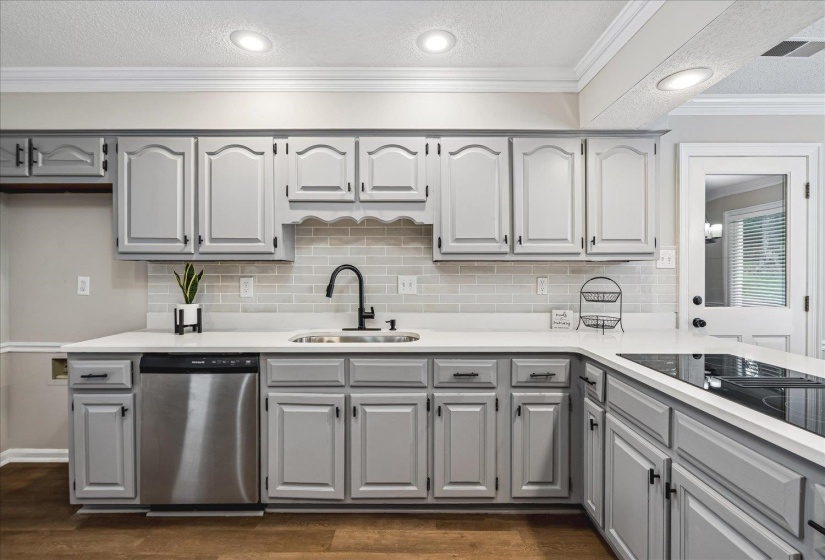 Kitchen featuring light gray cabinetry, stainless steel dishwasher, white countertops, glass tile backsplash, and wood-finish flooring