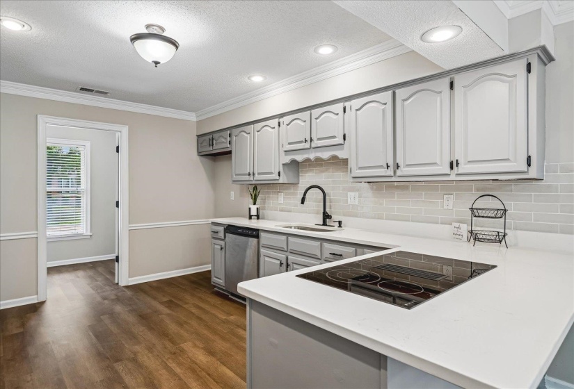 Kitchen featuring white shaker-style cabinetry, light solid surface countertops, a mosaic tile backsplash, and wood-finish flooring