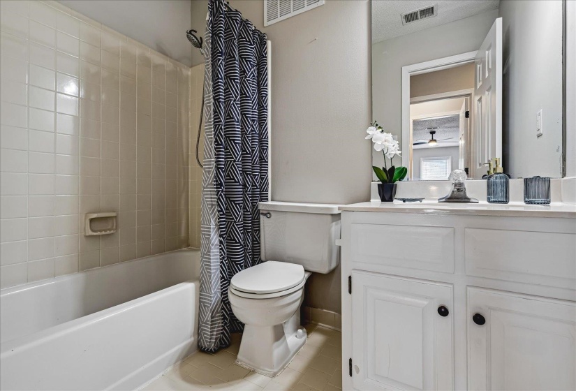 Bathroom featuring a white vanity with cabinet storage, a built-in bathtub with shower, ceramic tile walls, and a large wall-mounted mirror