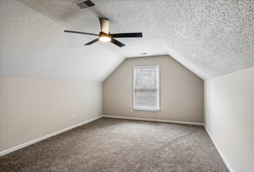 Carpeted room featuring an angled ceiling, a centered window with horizontal blinds, and a modern ceiling fan with integrated lighting