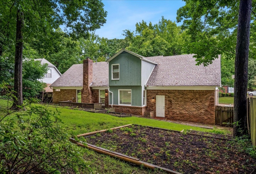Rear elevation featuring brick and siding finishes, a prominent brick chimney, and mature surrounding trees