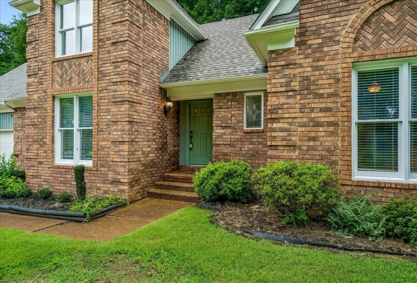 Brick exterior featuring herringbone pattern accents, a green entry door, and white frame windows