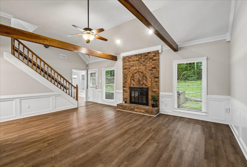 Spacious living area featuring wood-finish flooring, a brick fireplace with an arched hearth, and a vaulted ceiling with exposed wood beams