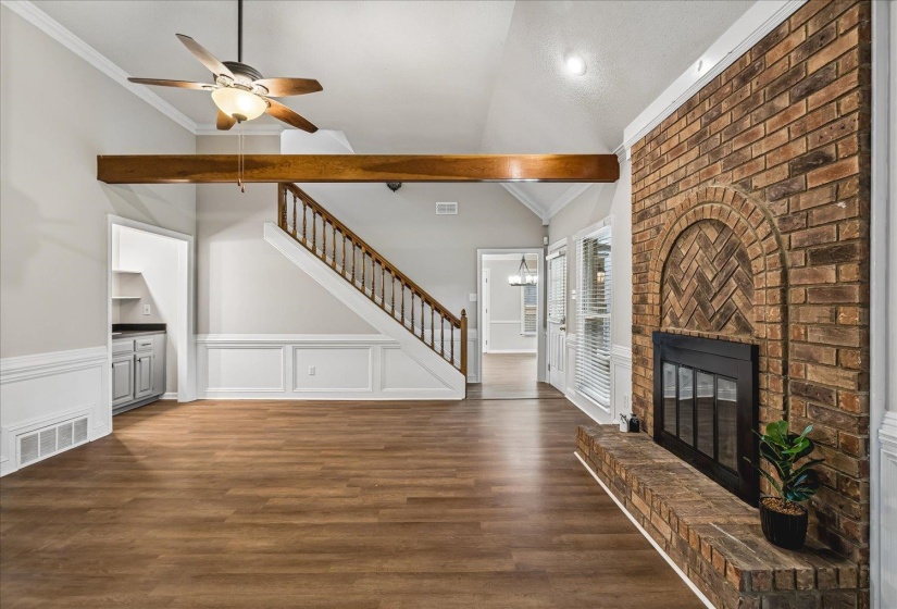 Living area featuring a floor-to-ceiling brick fireplace with a chevron pattern, wood-finish flooring, a vaulted ceiling, and a prominent wood beam