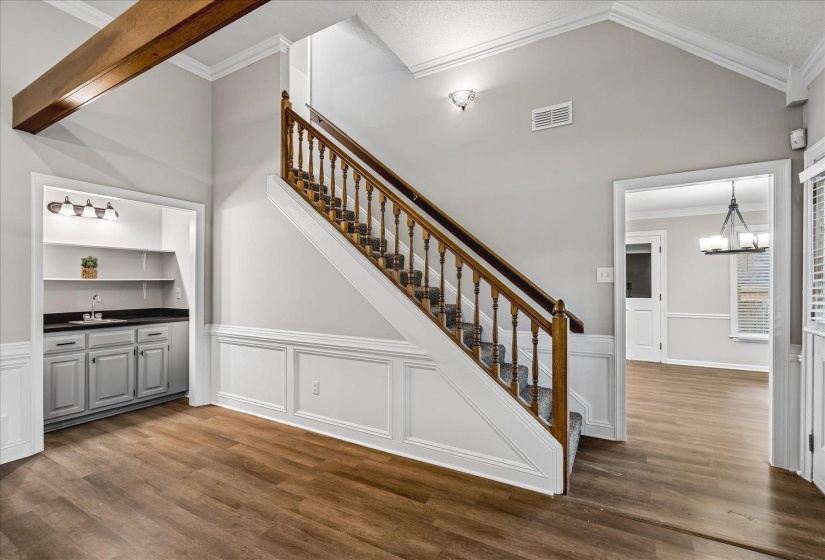 Interior featuring a prominent wooden staircase with carpeted treads and white wainscoting