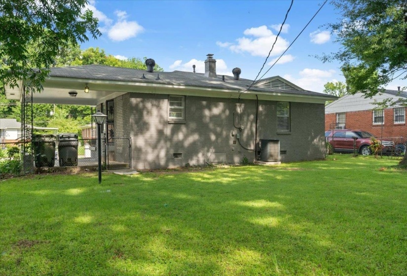 Expansive rear yard featuring a manicured lawn, mature trees, and a covered patio